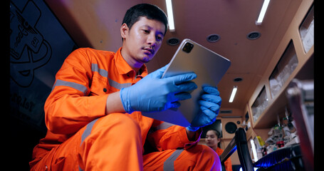 Asian man emergency medical technician (EMT) or paramedic nurse using tablet in ambulance car