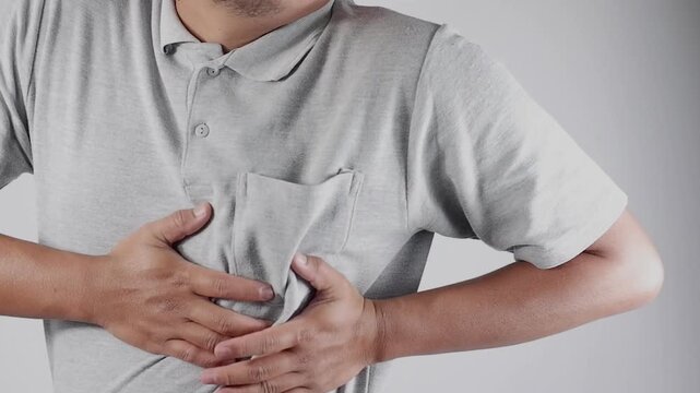 A young man in a gray shirt is holding his left chest with severe heart pain. Due to heart disease. Heart attack problems. Warning signs of a terrible disease. Health care.