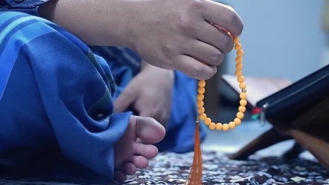 Close-up of hands reciting dhikr using prayer beads with a blurred background. Hands reciting dhikr. A man reciting dhikr while holding a prayer bead. Front view photo
