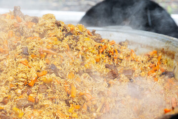 Central Asian plov or pilaf cooking in a large cauldron, steaming and ready to serve