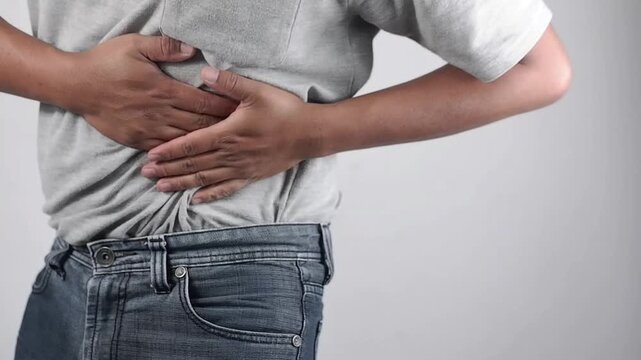 Sick Asian man experiencing abdominal pain, pain and discomfort, severe abdominal pain, left kidney infection or appendicitis, pain in the left side of the abdomen, squeezing the abdomen with an expre
