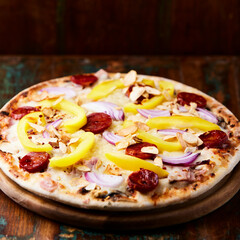 Pizza with chorizo ​​sausage, mozzarella cheese and yellow pepper. Rustic wooden background. Soft focus.	