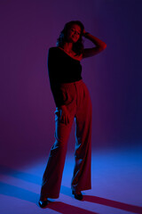 Model poses confidently in dramatic lighting with purple and blue hues at a stylish studio