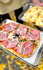 Roman pizza with Vitello Tonato and 4 cheeses, prepared for Halloween and decorated with a spider web and mushroom skulls. The chef holds two trays.