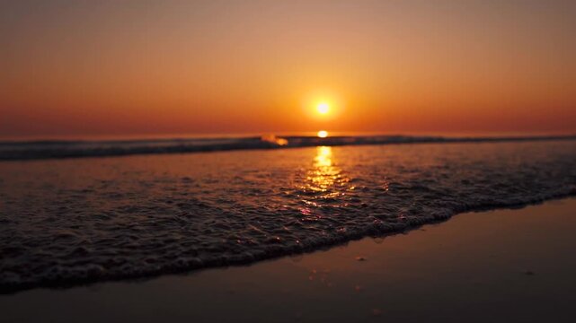 Low angle shot of sunset at beach in Mandvi, Kutch, India. Small ocean waves crashing on shore. Orange color clear sky and setting sun. Nature landscape. Travel and summer holidays background.