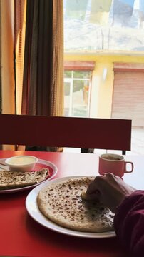 4K POV shot of Indian girl eating Paratha in local restaurant in mountain village near Keylong, Lahaul, India. Local Indian food, healthy breakfast with hot tea. Healthy homemade food concept. 