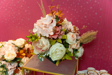 Beautiful bouquet featuring peonies and hydrangeas in soft hues is arranged on a stand, creating a vibrant centerpiece against a bright pink backdrop.