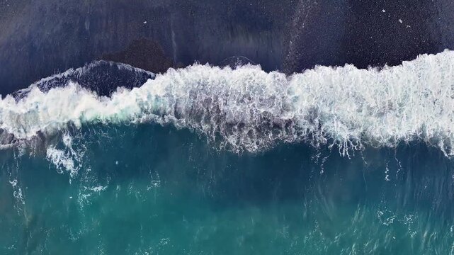 Aerial looking down at waves on a black sand beach in Bali Indonesia.