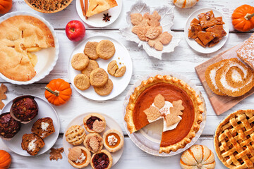 Autumn desserts table scene. Table scene with a collection of traditional fall sweet treats. Above view over a white wood background. Copy space. Pies, pumpkin roll, muffins, cookies.