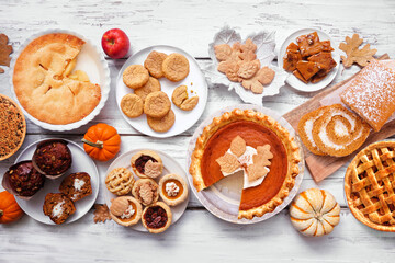 Autumn desserts table scene. Table scene with a collection of traditional fall sweet treats. Above view over a white wood background. Copy space. Pies, pumpkin roll, muffins, cookies.