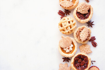 Fall pie theme dessert side border. Top down view against a white marble background. Pumpkin, apple and pecan mini pies.