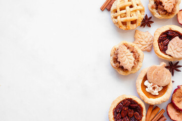 Autumn pie theme dessert side border. Overhead view against a white marble background. Pumpkin, apple and pecan mini pies.