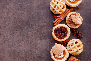 Autumn pie theme dessert side border. Top view against a dark stone background. Pumpkin, apple and pecan mini pies.