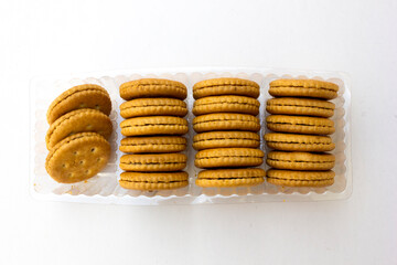 Several stacks of golden crackers in the transparent container, isolated on white background, showcasing their round shape and crispy texture. 