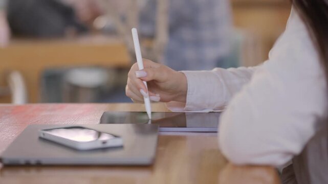 Person is writing on a tablet with a pen. A cell phone is on the table next to the tablet