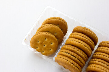 Several stacks of golden crackers in the transparent container, isolated on white background, showcasing their round shape and crispy texture. 