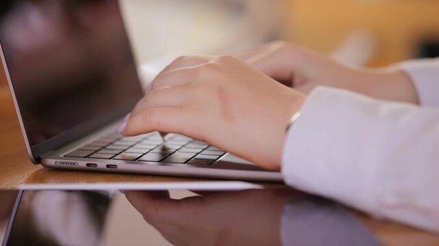 Woman is typing on a laptop. She is wearing a white shirt. The laptop is open and the screen is on