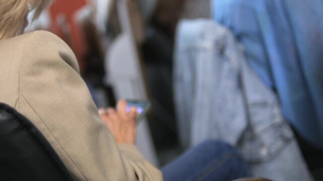 Woman is sitting on a chair and using her cell phone. A backpack is on the floor in front of her