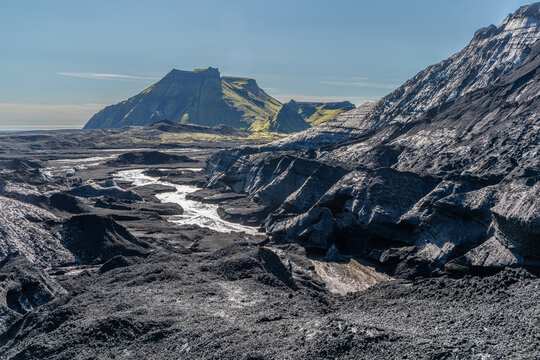 Glacier de K&ouml;tluj&ouml;kull &agrave; la glace noire et bleue, dans le sud de l'Islande, avec les falaises couvertes de mousse et de verdure de V&iacute;k &iacute; M&yacute;rdal et l'oc&eacute;an au loin