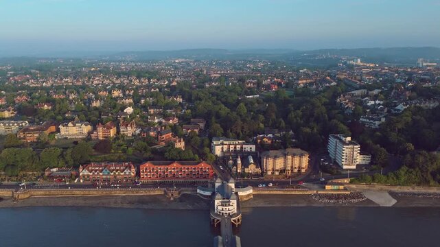 Aerial drone footage of Penarth seafront at sunrise overlooking the pier and residential areas. High altitude revealing pull out shot.
