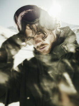 Young male athlete in winter clothing and sporty ski goggles standing at the top of a mountain slope. Active mountain recreation and winter sports training.