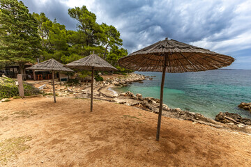 Tara Beach, Rab, sun umbrellas on the shore of the Adriatic Sea, cloudy, threatening sky, azure water