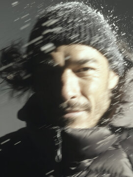 A man with a mustache in a black winter jacket walking in the middle of a snowstorm. An athlete on a snowy slope during training.
