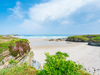 Playa des Catedrales in Galicia Spain sandstone rocks tidal pools sky cliffs wide shore under bright light clear blue sky peaceful calm natural wonder