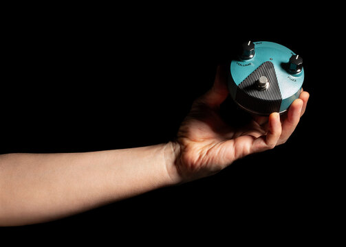 guitar fuzz pedal in hand on black background