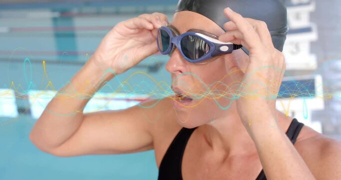 Mature competitive swimmer lifting goggles at pool edge, adjusting strap for lap swimming training
