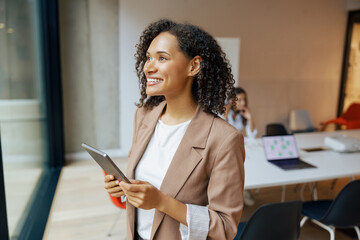 A professional woman beams with a smile while confidently holding a tablet in a fashionable office space