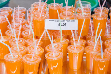 Plastic cups of mango and passion fruit juice with straws are displayed for £1 at Brick Lane...