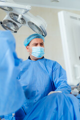 Surgeon operating in a modern healthcare facility. In a surgical room, a focused surgeon in blue scrubs prepares for a procedure, monitored by medical equipment.
