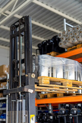 Forklift lifting pallet of metal cylinders in warehouse. A forklift lifts a wooden pallet of metal cylinders in a busy warehouse with shelves of supplies behind.