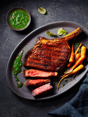 Steak Tomahawk with chimichurri sauce on a black plate. Dark background. Top view.