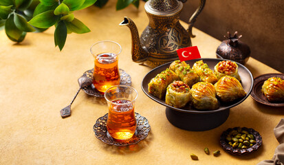 Baklava dessert with Turkish flag on a stand served with tea in armudu glass from a copper teapot. Yellow and brown background. Close up.