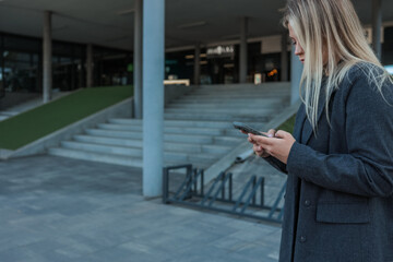 Fototapeta premium Woman using smartphone outdoors near building