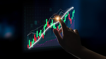 A hand interacts with a glowing digital financial chart, showcasing upward trends and candlestick...