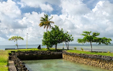 A scenic view of the coastline on Koror island, Palau, featuring a stone inlet, green trees, and the Pacific Ocean under a cloudy sky