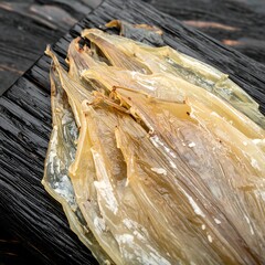 Dried fish, light beige, stacked, on dark wood