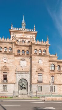 Panorama showing Cavalry Academy facade timelapse in Plaza de Zorrilla, Valladolid, Spain. Historic military building with intricate architecture, surrounded by busy urban scene under blue cloudy sky