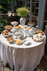 Outdoor vintage tea table with traditional Russian sweets, baranki, and chamomile bouquet in a porcelain vase, set against a wooden terrace