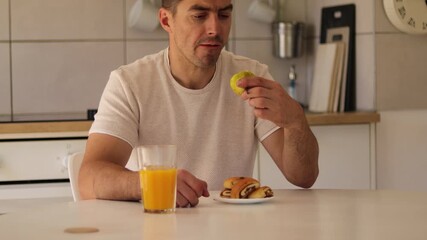A man sits at his kitchen table, appreciating a ripe pear while drinking orange juice. He takes a moment to savor his breakfast, embracing a healthy lifestyle at home