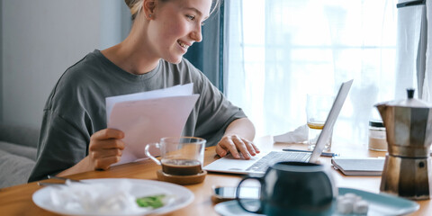  Gen Z woman working from home at cozy kitchen table with laptop and phone. Digital nomad lifestyle, mindfulness, remote work, balance, mental calm and modern freelancing