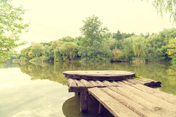 Obraz premium Wooden pier on calm lake with forest reflection. Landscape photography with copy space. Nature, travel, and outdoor recreation concept. Design for postcard, greeting card, banner, poster, wallpaper