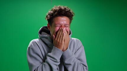 Man in gray hoodie laughing heartily against green screen.