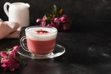 Pink matcha latte with powder decorated sakura flowers on dark black background. Trendy beverage. Caffeine free. Close up.