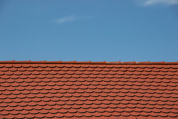 Red tiled roof with a textured surface against a clear blue sky, showcasing architectural design and craftsmanship in residential construction and home aesthetics