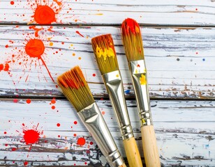 Paintbrushes with vibrant red splatters on a weathered wooden surface