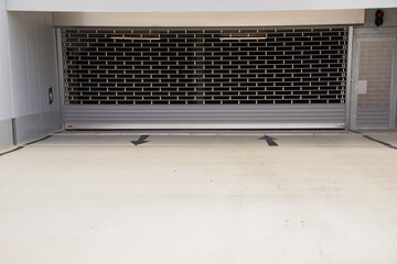 Industrial garage entrance with a closed metal shutter, featuring a smooth concrete floor and directional arrows, creating a modern urban atmosphere with a sense of security and functionality